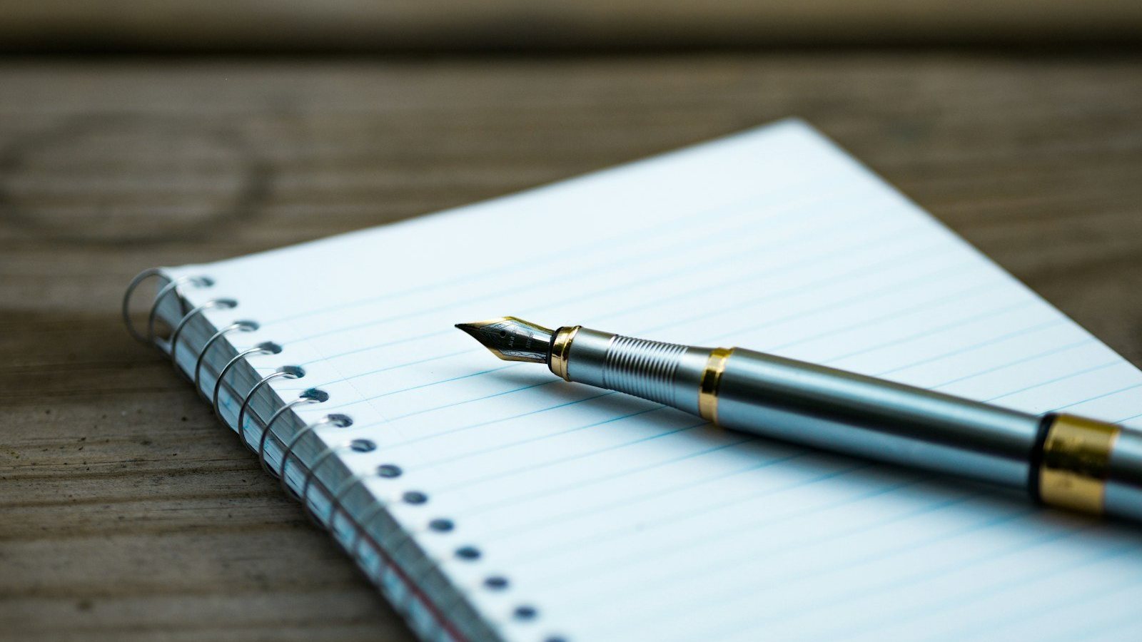 Pluma estilográfica sobre un cuaderno de espiral abierto en una mesa de madera