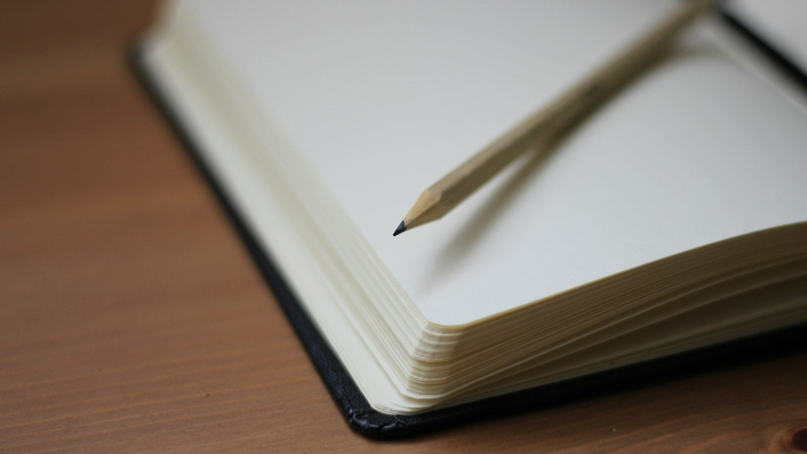 Cuaderno abierto con las páginas en blanco y un lápiz sobre una mesa de madera
