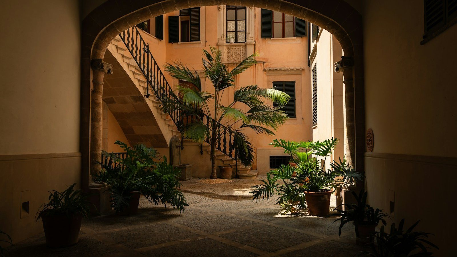Patio mediterráneo con escalera, arco y macetas con plantas verdes