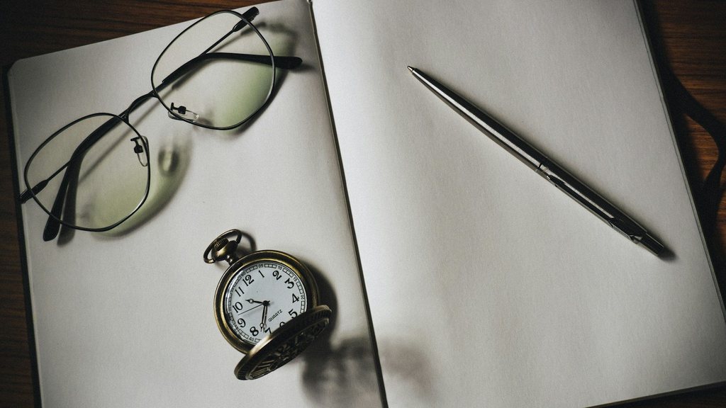 Cuaderno en blanco con gafas, reloj de bolsillo y bolígrafo sobre una mesa de madera