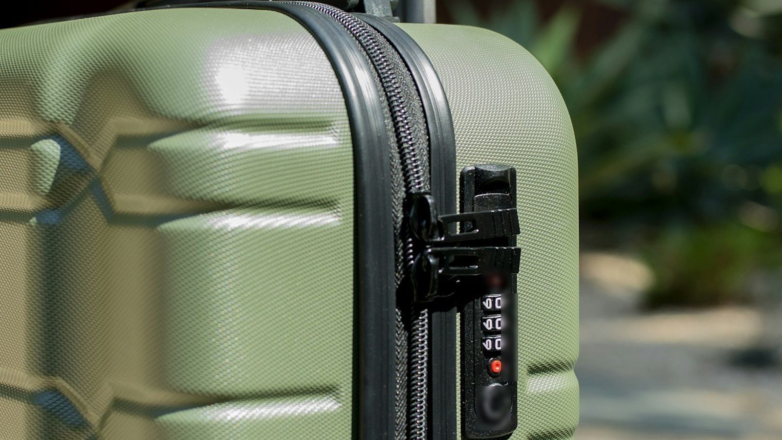 Maleta verde con candado junto a un jardín, lista para un viaje
